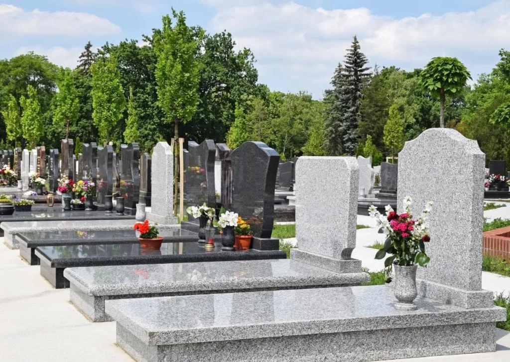 Alignement de tombes et monuments funéraires en granit gris et noir dans un cimetière bordé d'arbre